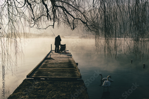 Fotografi Mysterious lake on an early winter morning photographed in backlight in central