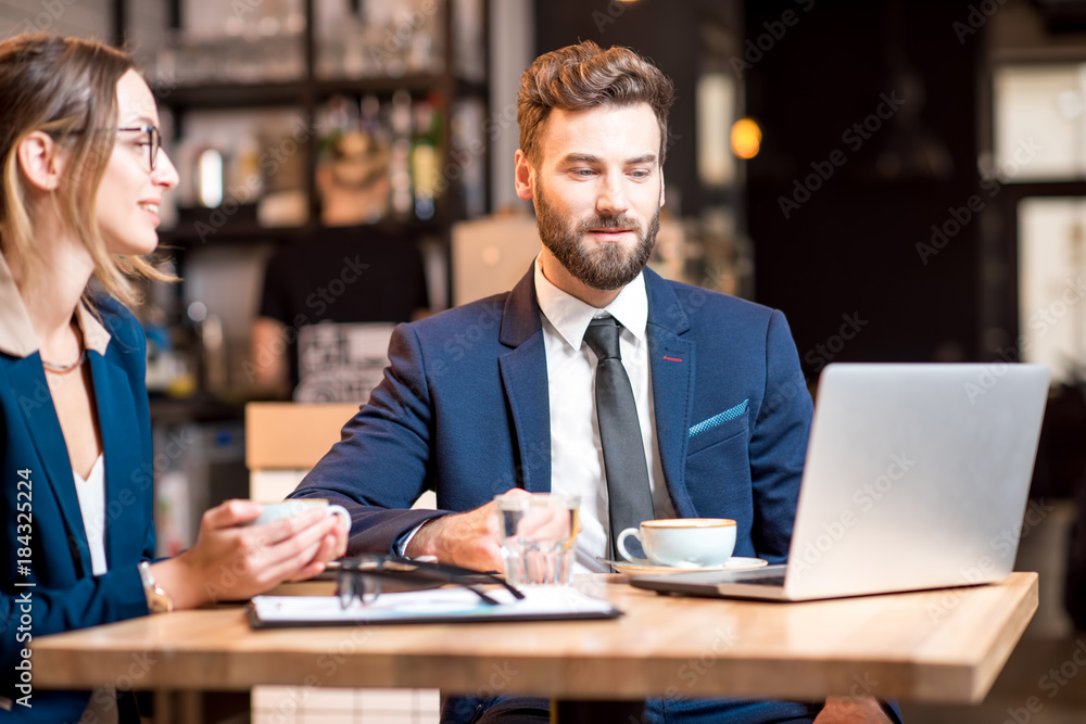Conversation between business couple dressed in suits sitting with coffee and laptop at the cafe or restaurant