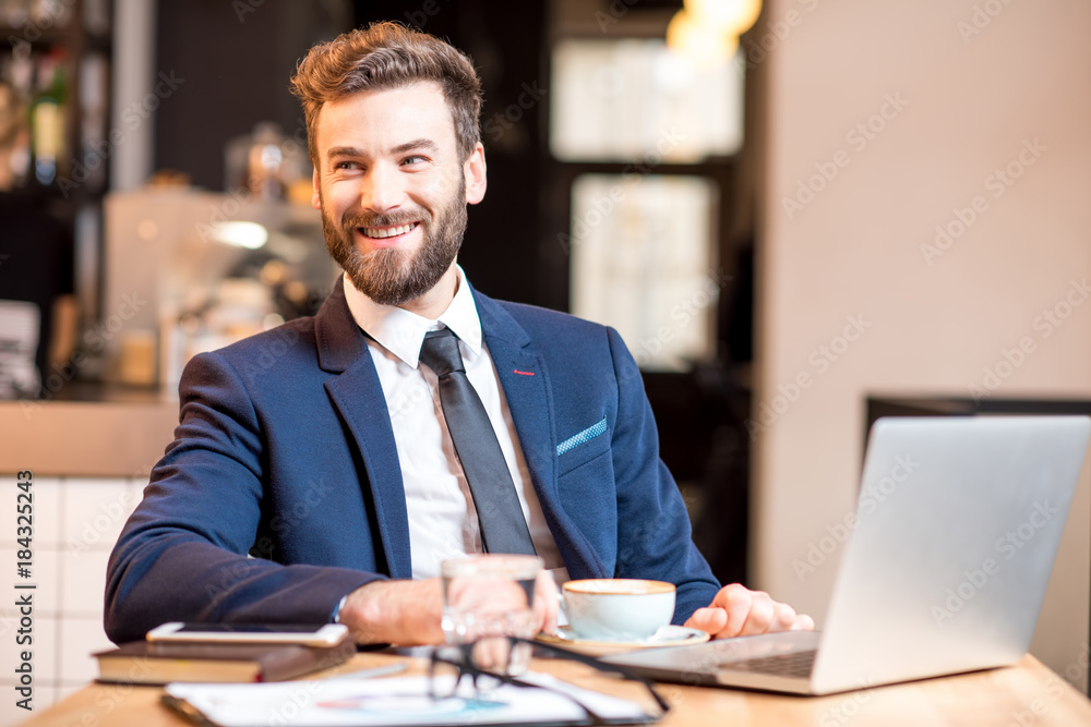 Portrait of a handsome businessman stricly dressed in the suit working with laptop at the modern cafe interior Portrait of a handsome businessman stricly dressed in the suit working with laptop at the modern cafe interior