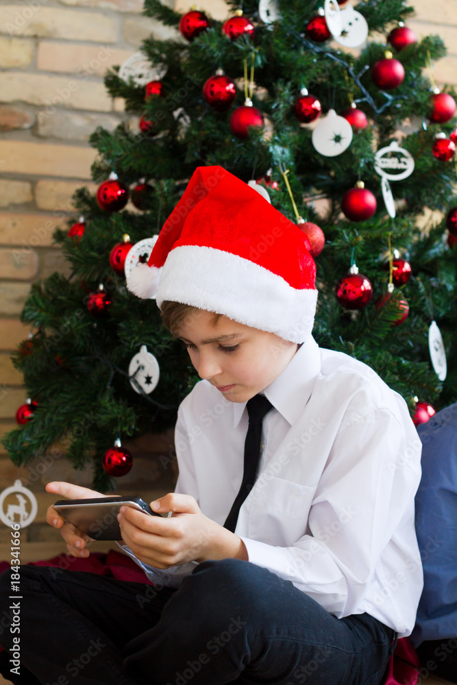 boy wearing a Santa hat and playing with tablet pc near a Christmas tree boy wearing a Santa hat and playing with tablet pc near a Christmas tree