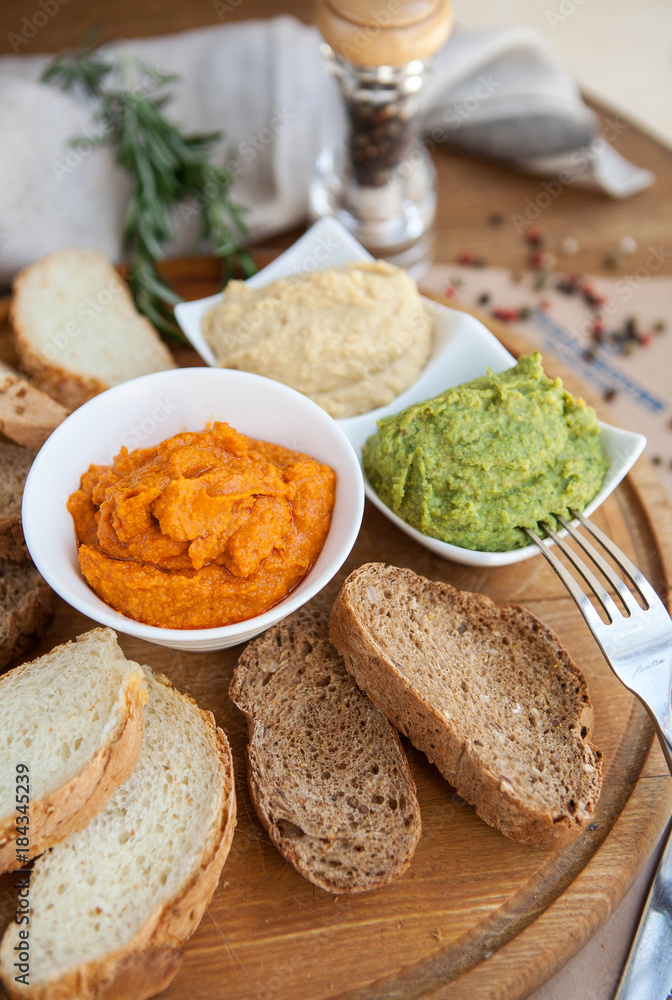three different kind of hummus : hummus of spinach, hummus paprika and classic hummus with bread sliced on a wooden board