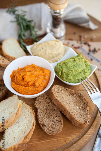 three different kind of hummus : hummus of spinach, hummus paprika and classic hummus with bread sliced on a wooden board