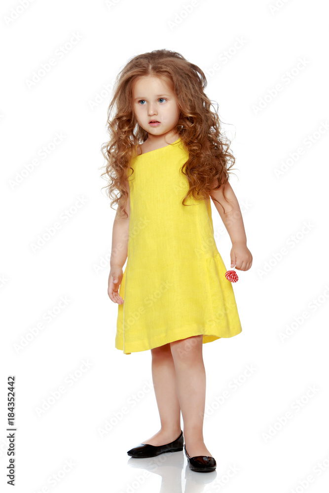 A little girl licks a candy on a stick. A little girl licks a candy on a stick.
