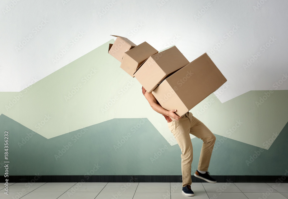 Man with moving boxes near color wall - obrazy, fototapety, plakaty 