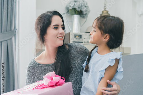 Mother giving a christmas gift to her daughther who hug her mom have funny on sofa in the living room photo