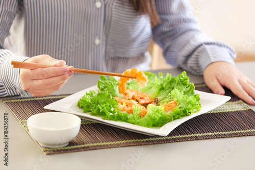 Young woman eating shrimps at table