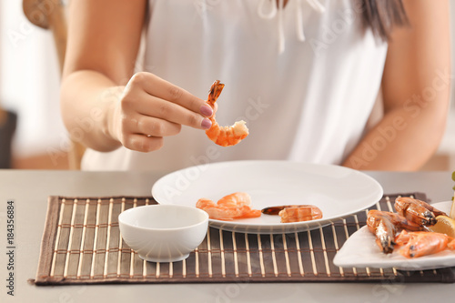 Young woman eating shrimps at table
