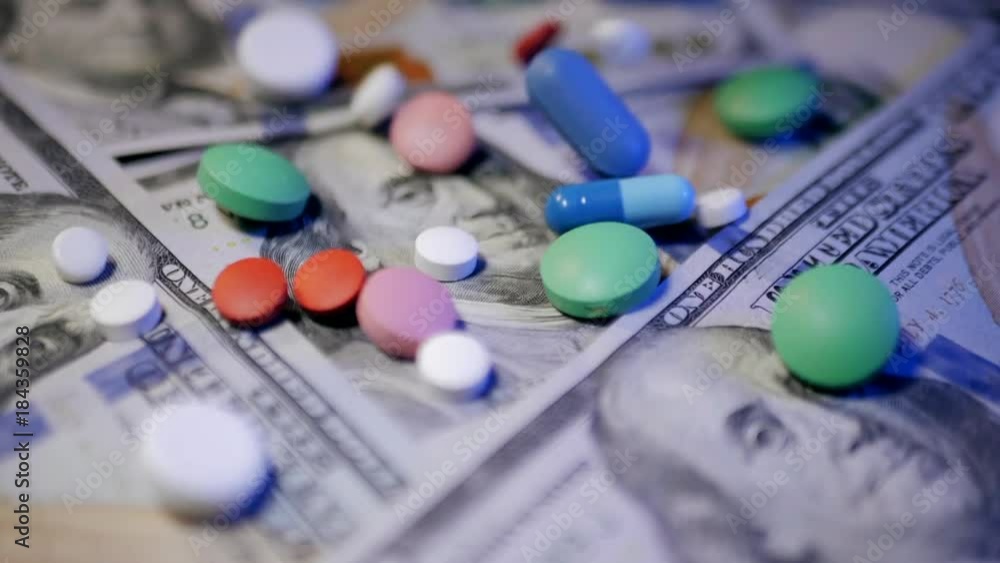 Pills falling on dollar banknotes, expensive medication, pharmaceutical business. Pharmacy theme. Multicolored Pills and Capsules on money. Slow motion. Pills falling on dollar banknotes, expensive medication, pharmaceutical business. Pharmacy theme. Multicolored Pills and Capsules on money. Slow motion.