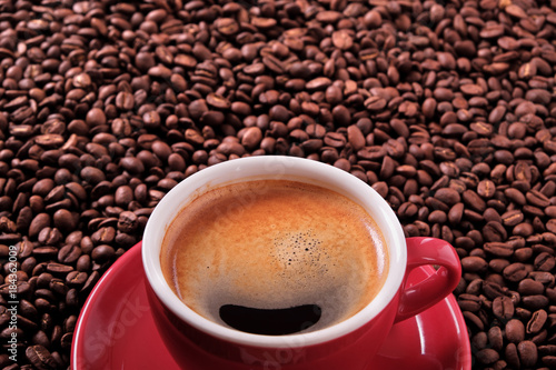 Red coffee cup and saucer one single for espresso or capuccino on a background of scattered dark coffee beans photo