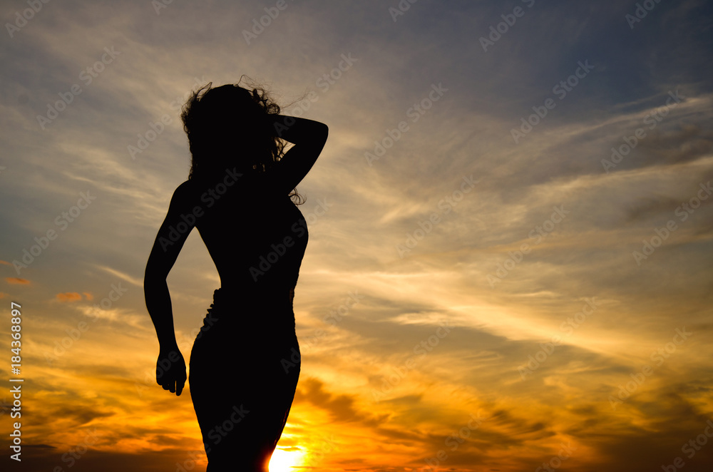 Silhouette of woman sitting on rock at sunset