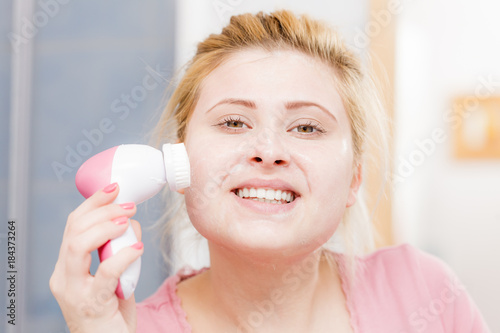 Happy woman using facial cleansing brush
