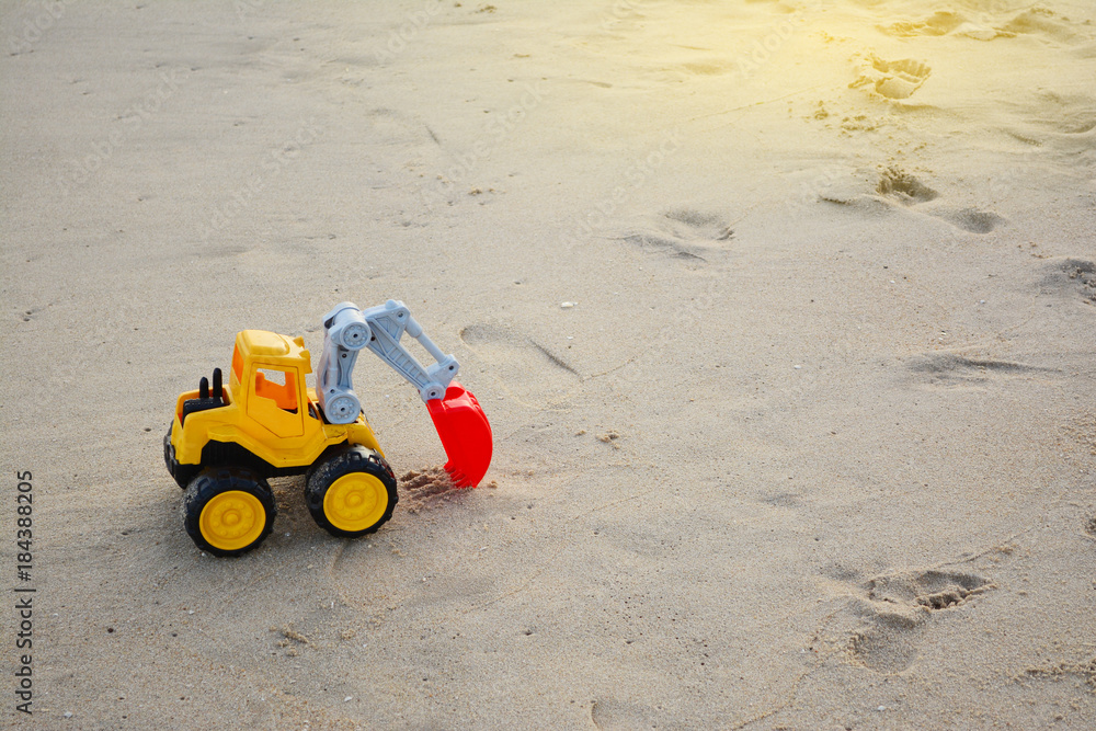 Children's toy excavator car on sand beach background or Yellow toy backhoe excavator on the playground sand Children's toy excavator car on sand beach background or Yellow toy backhoe excavator on the playground sand