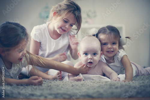Little baby brother with sisters poses to camera.