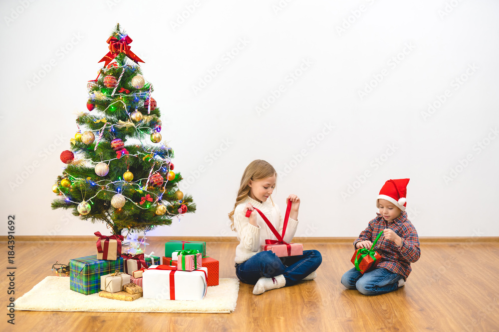 The boy and a girl unpack gift boxes near the christmas tree