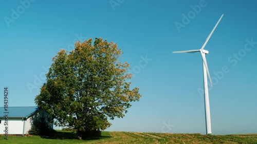 Independent power supply of a house or a farm. Wind generator near the building, a tree is growing nearb photo