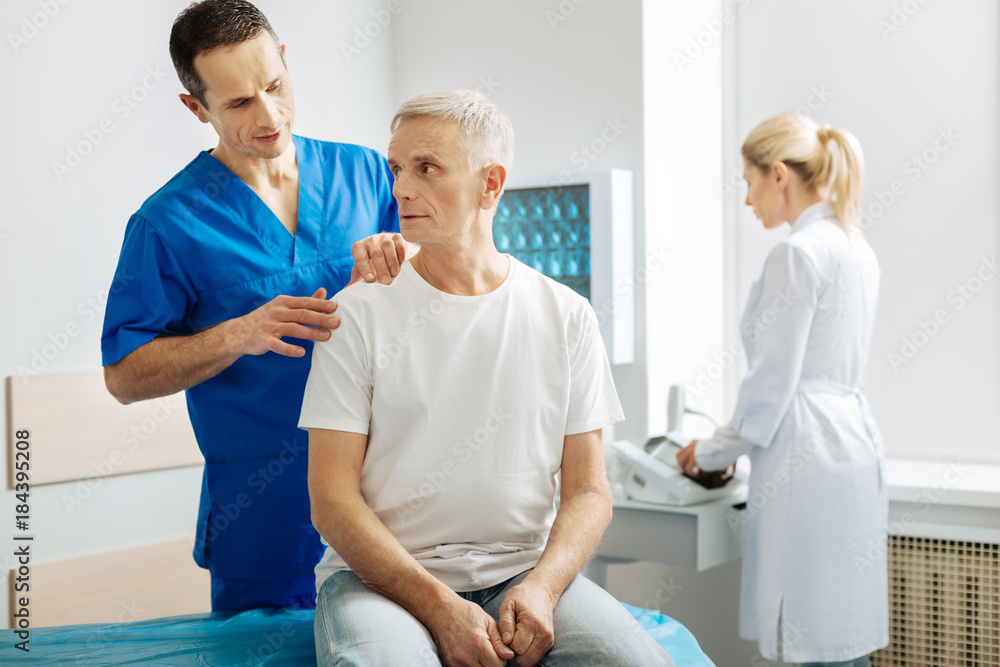Describe your feelings. Smart handsome nice man standing behind his patient and touching his shoulder while asking hem to describe what he feels Describe your feelings. Smart handsome nice man standing behind his patient and touching his shoulder while asking hem to describe what he feels