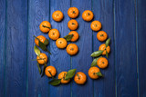 orange juicy mandarins (mandarins) with green leaves on a blue wooden background lined in the form of a clock showing that the new year is coming soon