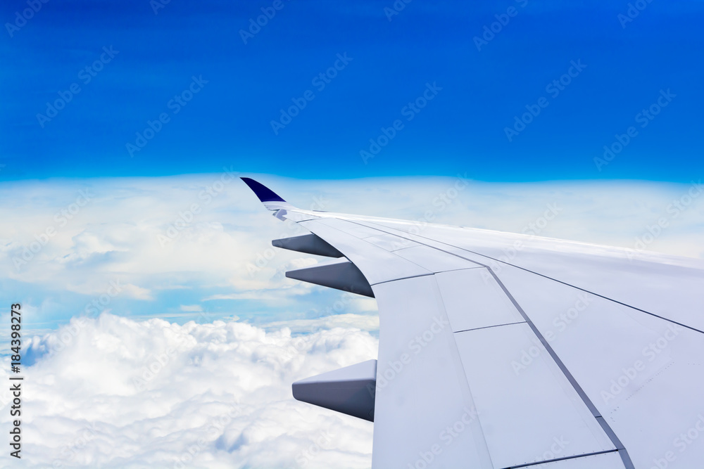 The wing looks out of the plane window. While flying over the white clouds and overlooking the horizon and blue sky. Free space for text and more.