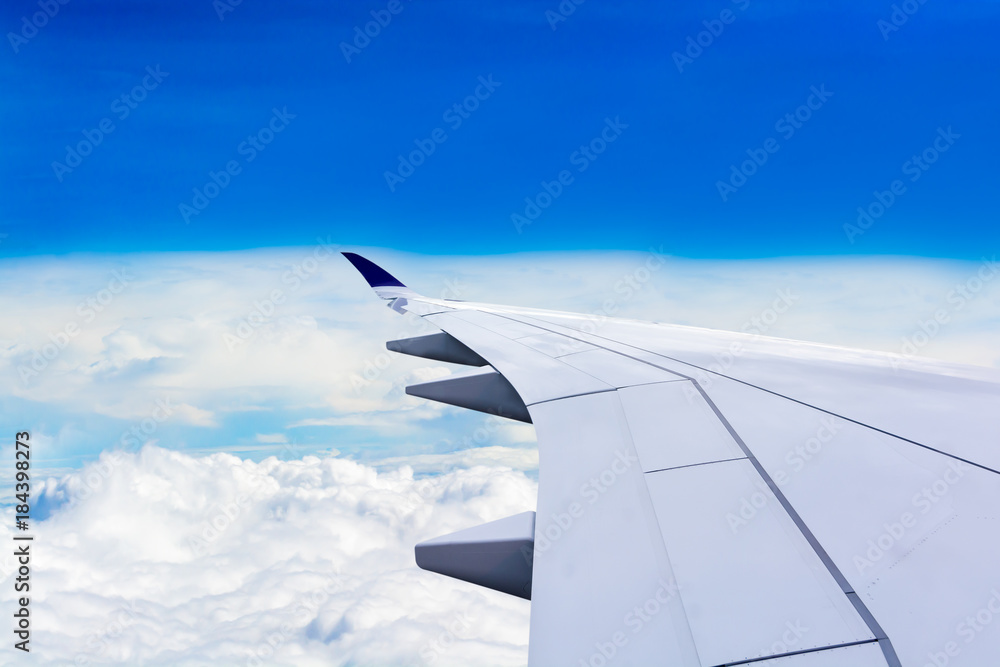 The wing looks out of the plane window. While flying over the white clouds and overlooking the horizon and blue sky. Free space for text and more. The wing looks out of the plane window. While flying over the white clouds and overlooking the horizon and blue sky. Free space for text and more.