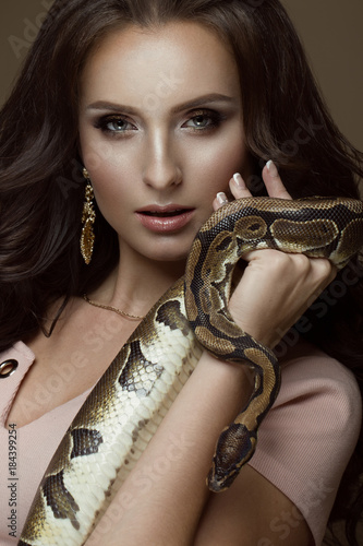 Beautiful girl brunette model, perfect curls and evening fashion make-up with a snake in her hands. Beauty face. Picture taken in the studio on a black background.