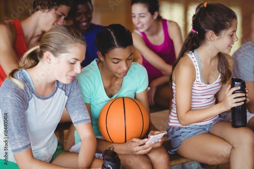 High school kids using mobile phone while relaxing in basketball
