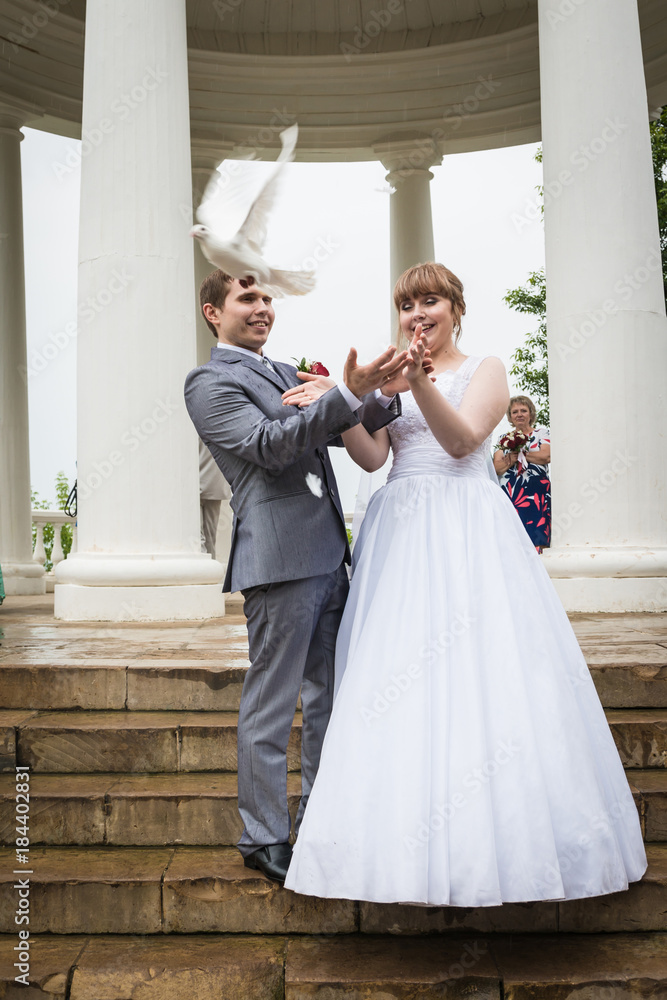 Bride and groom near the white columns and the pigeons in their hands