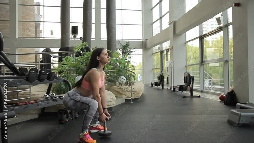 Female athlete is squatting with dumbbell in gym. Woman holds free weight. Female athlete is squatting with dumbbell in gym. Woman holds free weight.