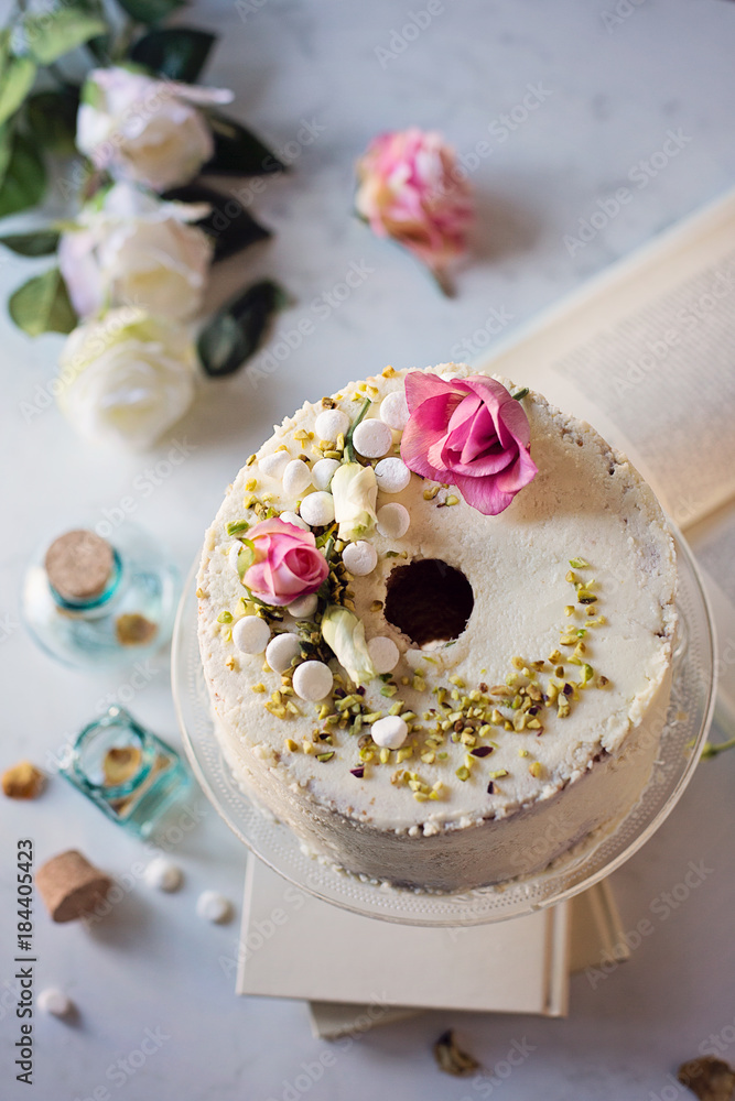 Foto Stock Chiffon cake con cioccolato bianco decorata con pistacchi,  meringhe e petali di rosa su tavolo di marmo | Adobe Stock