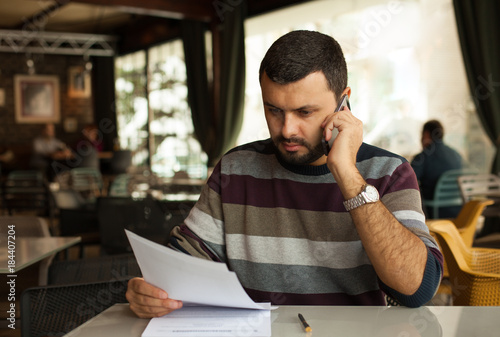 Handsome man using phone and looking at papers