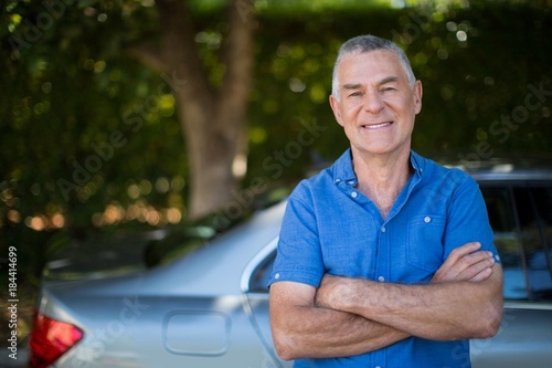 Senior man with arms crossed standing by car