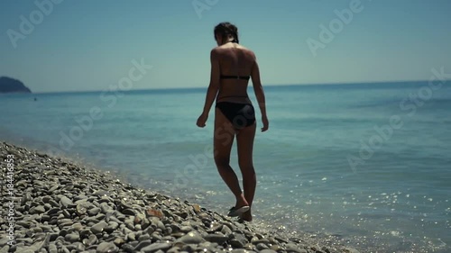 A slender girl in a swimsuit, walking along the beach with pebbles near the blue sea. HD, 1920x1080. slow motion. photo