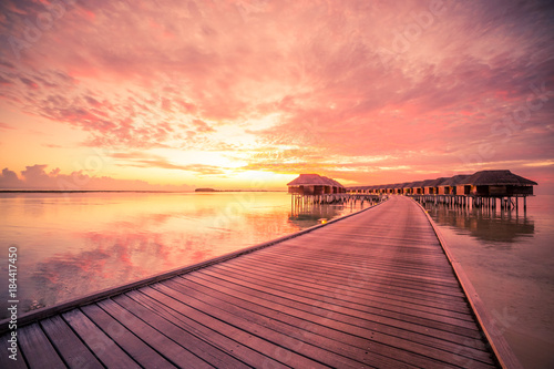 Fototapeta Naklejka Na Ścianę i Meble -  Sunset on Maldives island, luxury water villas resort and wooden pier. Beautiful sky and clouds and beach background for summer vacation holiday and travel concept
