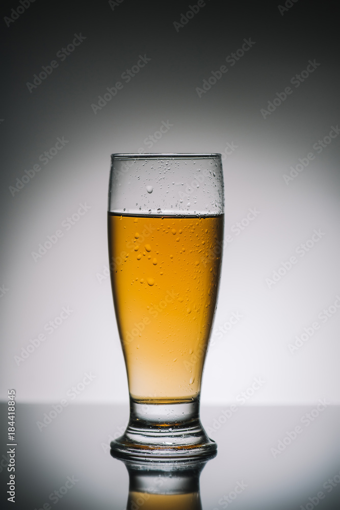 single glass with light fresh beer on gray reflecting table single glass with light fresh beer on gray reflecting table