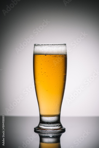 glass with light beer with foam on gray reflecting surface