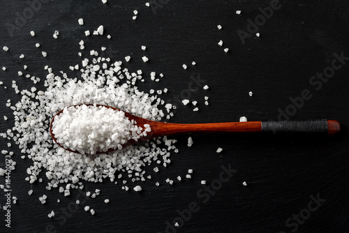 Sea Salt in Bamboo Wooden Spoon on black stone background