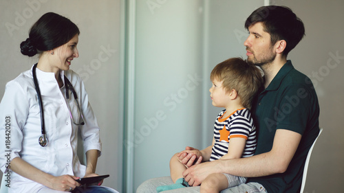 Young woman doctor talking with father of little boy in medical office