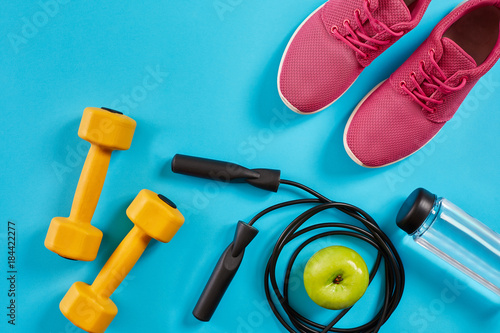 Flat lay of female sport equipments, jump rope, bottle of water and pink sneakers on blue background © nazarovsergey
