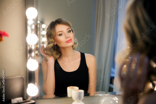 Fotografie Attractive blonde girl primp at the mirror with lamps in the beauty studio