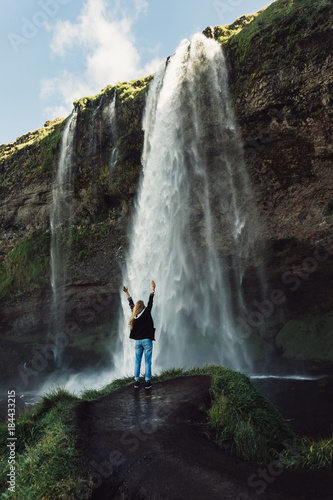 back view of young woman standing with raised hands and looking at beautiful waterfall in Iceland