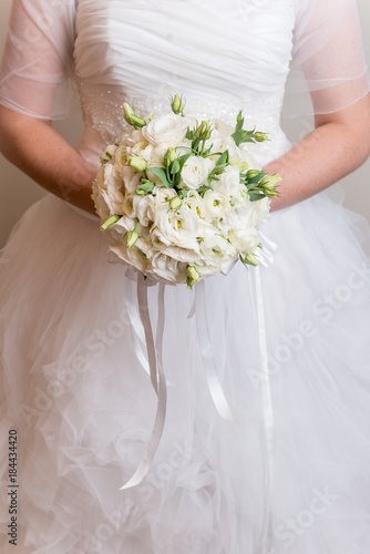 Sposa in abito bianco che tiene fra le mani un bouquet rotondo di rose bianche