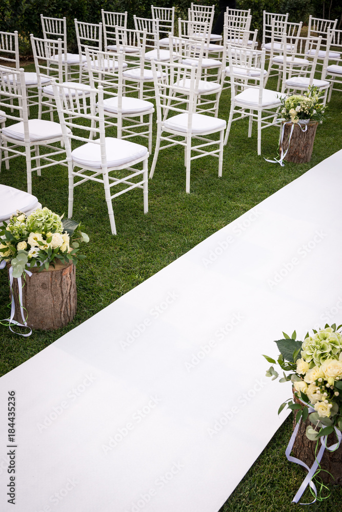 File di sedie bianche allineate e tappeto passatoia bianco sul prato  addobbato con composizioni floreali per un matrimonio Stock-Foto