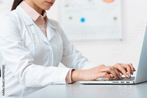 cropped shot of doctor in white coat working on laptop in clinic