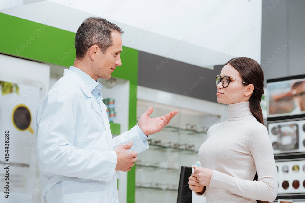 Obraz premium side view of oculist and young woman having conversation in optics