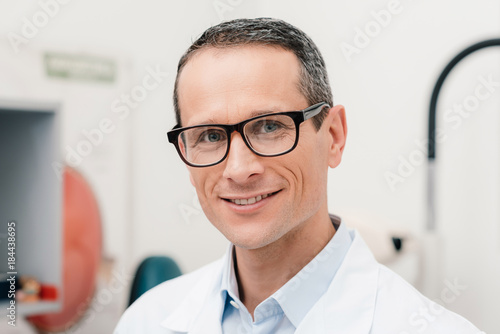 portrait of smiling doctor in eyeglasses looking at camera in clinic