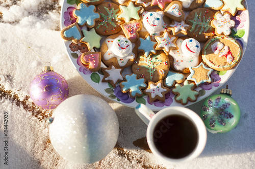 Имбирное печенье в форме звездочек, цветов, сердечек, Санта Клауса и растаявших снеговиков на круглом блюде на снегу с шариками и чашкой чая