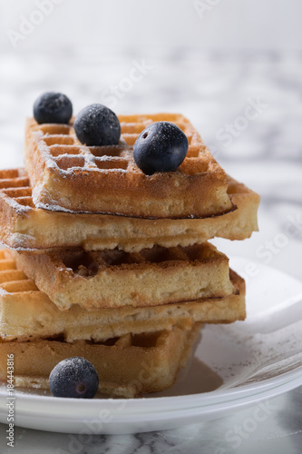 Waffles on a white plate decorated with blueberries with marbled background. copy space photo