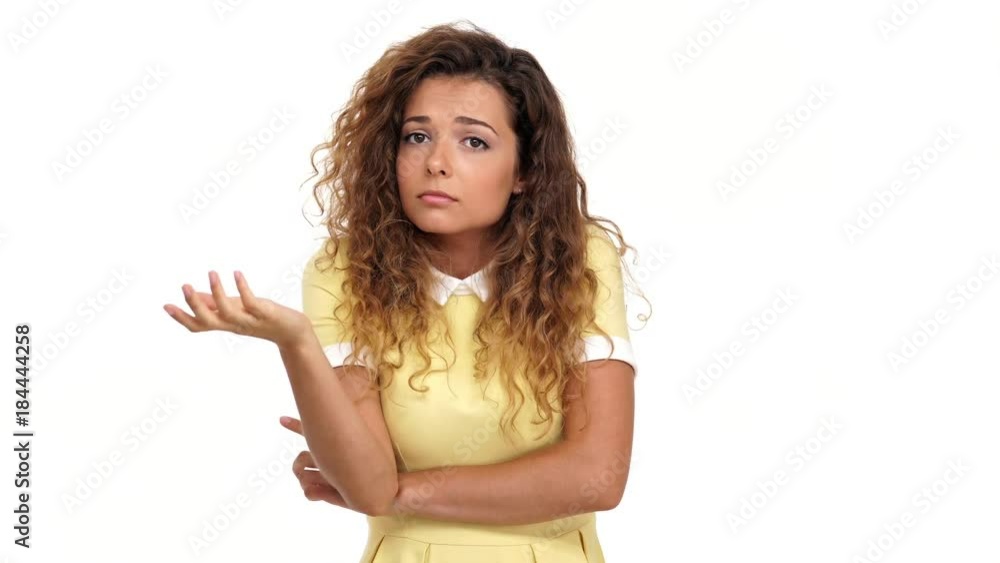 Pensive pretty curly brunette woman in dress shrugs her shoulders and unaware of the answer over white background Pensive pretty curly brunette woman in dress shrugs her shoulders and unaware of the answer over white background