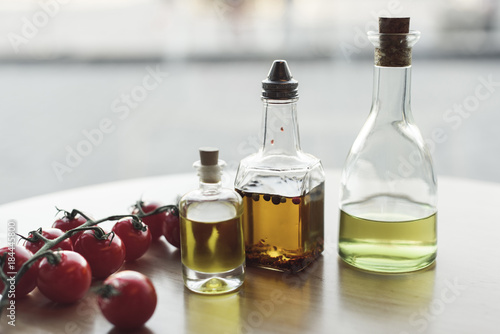close up view of various types of oil in bottles and fresh cherry tomatoes