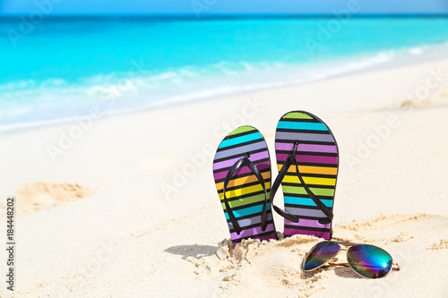 Multicolored flip-flops and sunglasses on a sunny beach..Tropical beach vacation and travel concept.