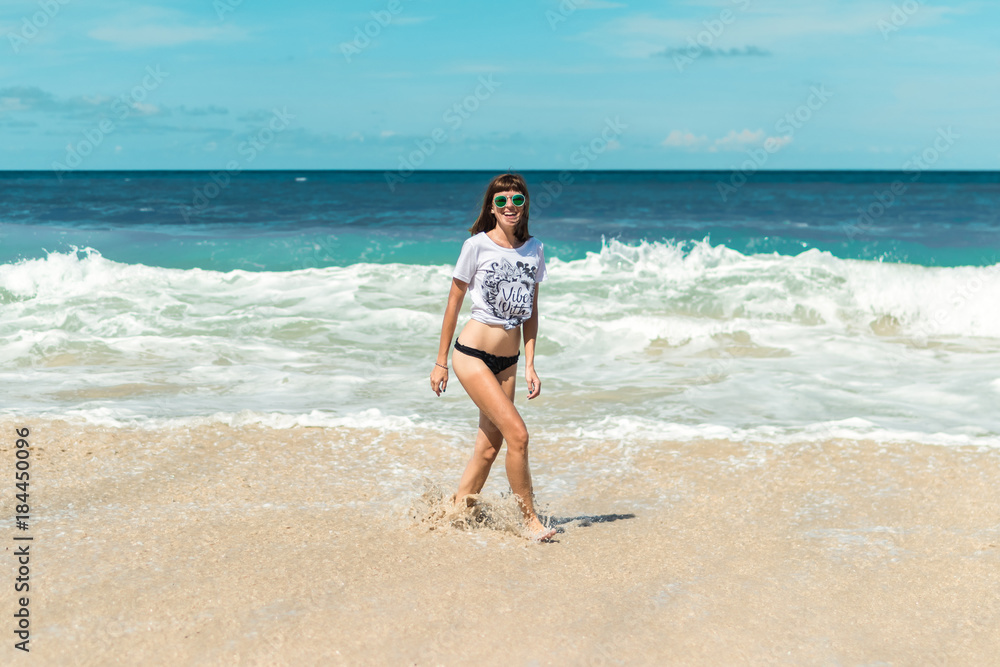 Beautiful young woman in sunglasses posing on the beach of a tropical island of Bali, Indonesia.